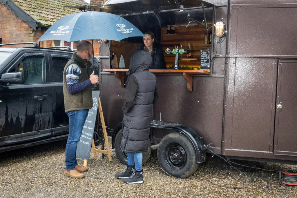 Visitors at the horsebox bar, sheltering under umbrellas at the Ashdon Christmas Market