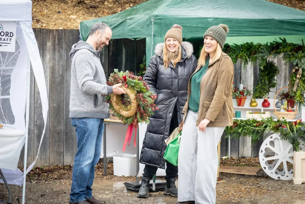 Shoppers laughing with a stallholder holding a Christmas wreath at the Ashdon Christmas Market
