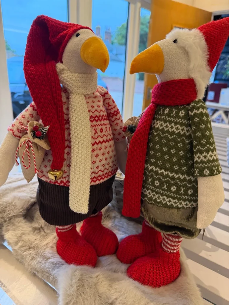 Two soft toy geese in Christmas jumpers, scarves and red hats